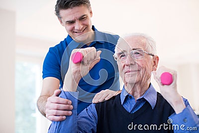 Physiotherapist Helping Senior Man To Lift Hand Weights Stock Photo