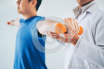 Physiotherapist man giving exercise with dumbbell treatment About Arm and Shoulder of athlete male patient Physical therapy Stock Photo