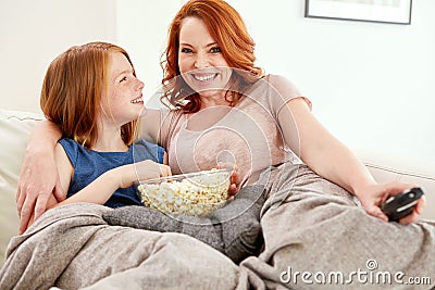 She picked tonights movie. a mature woman and her young daughter watching a movie and eating popcorn on the sofa. Stock Photo