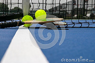 Pickleball paddles and two yellow whiffle balls on a blue court on white line Stock Photo