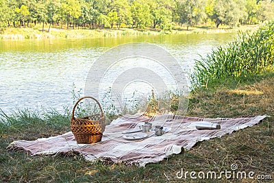 Picnic set, metal Cutlery, thermos, plates tea cups. brown plaid and napkin from the lake in the background. green grass. Sunny su Stock Photo