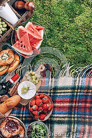 Picnic straw basket with healthy food, accessories. Summer picnic with cake, fruits, cheese, wine and snacks on plaid Stock Photo