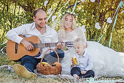 Picnic style outdoor wedding. Groom playing on guitar, young attractive blomde bride and little blond boy Stock Photo