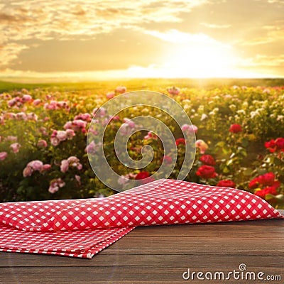 Picnic wooden table with checkered napkin and beautiful roses on background Stock Photo