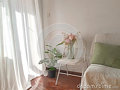 Picture captures a cozy bedroom, featuring two vibrant vases of flowers and a bright white chair Stock Photo