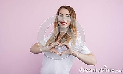 Picture of cheerful beautiful charismatic female looking directly at camera, making gesture, showing shape of heart with Stock Photo