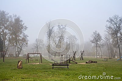 Wooden children playground, a play area made of slides and swings, empty, in a mysterious foggy misty smog, during a cold winter Stock Photo