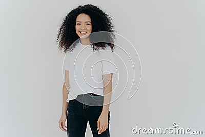 Picture of good looking woman with gentle smile, stands satisfied, has sincere carefree expression, relaxed casual mood, dressed Stock Photo