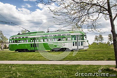 Green trolley driving past a park Editorial Stock Photo