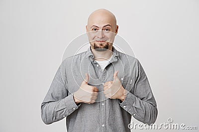 Picture of happy handsome guy in casual gray shirt holding his thumbs up in approving gesture over white background Stock Photo