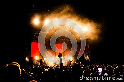 Picture of a lot of people enjoying night perfomance, large unrecognizable crowd dancing with raised up hands and mobile phones on Stock Photo