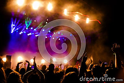Picture of a lot of people enjoying night perfomance, large unrecognizable crowd dancing with raised up hands and mobile phones on Stock Photo