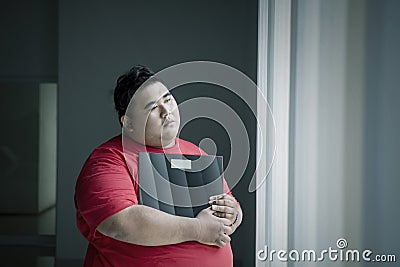 Pensive obese man holding a scale near the window Stock Photo