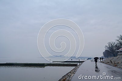 People walking with umbrellas near the Danube river during a heavily foggy and rainy winter afternoon in Zemun, Belgrade, Serbia Editorial Stock Photo