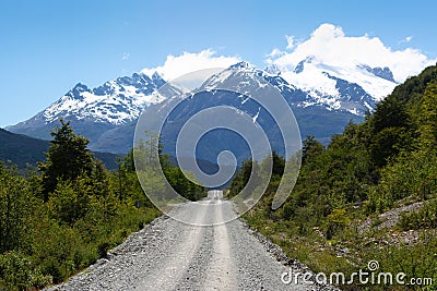 Picture of a road surrounded by beautiful greenery against mesmerizing snow-peaked mountains Stock Photo