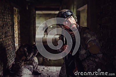 A picture of soldiers standing in dark corridor of empty building. Bearded guy is looking up and holding rifle. The Stock Photo