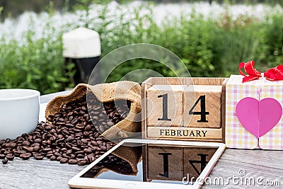 Picture of tablet, a cup of coffee, coffee beans and 14 February wooden calendar with Valentine concept Stock Photo