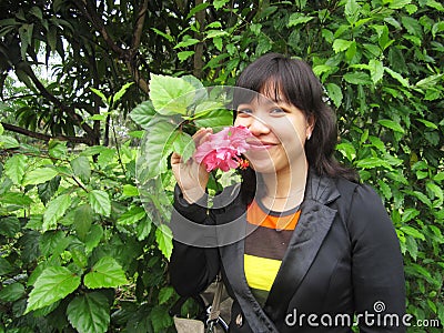 Beautiful woman kept a pink flower with happy face and green leaves around the background Stock Photo