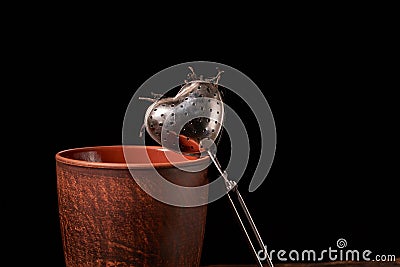 Picture of the tea strainer with dried tea leaves and sticks of cinnamon isolated on dark wooden background Stock Photo