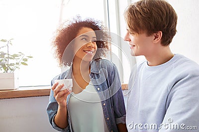 A picture of two students sitting together very close. Girl is holding a cup in her hands and looking at guy. He is Stock Photo