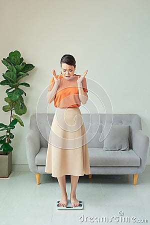 Picture of unhappy woman on scales in living room. Weight loss diet Stock Photo