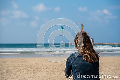 Picture of a woman on the beach looking at two kitesurfers in the sea Stock Photo