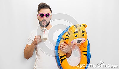 Picture of young bearded man standing and chilling. He drinks milk and hold kids matrass in hand. Guy wears sunglasses Stock Photo