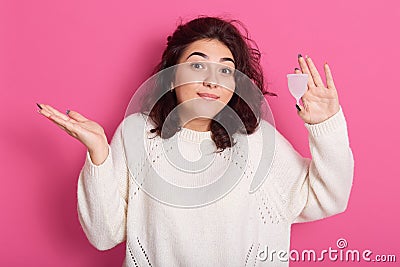 Picture of young brunette woman with wavy hair holding menstrual cup and squeesing her shoulders, does not know how to use Stock Photo