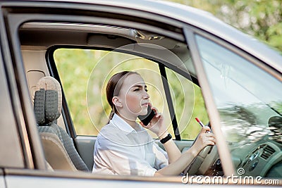 Picture of young businesswoman speaks by phone and doing makeup while driving a car in the traffic jam Stock Photo