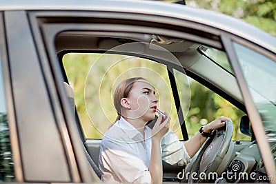 Picture of young businesswoman speaks by phone and doing makeup while driving a car in the traffic jam Stock Photo