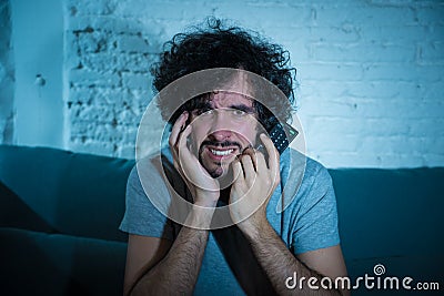 Picture of young man looking disgusted sitting on sofa watching violent movie on TV at night Stock Photo