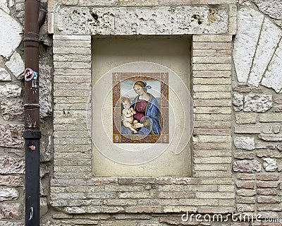 Art piece featuring the Madonna with the Child Jesus in an outside wall niche on a street in Assisi, Italy . Editorial Stock Photo