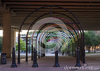 Walkway under a freeway in downtown dallas, with multi-colored lights in arches. Stock Photo