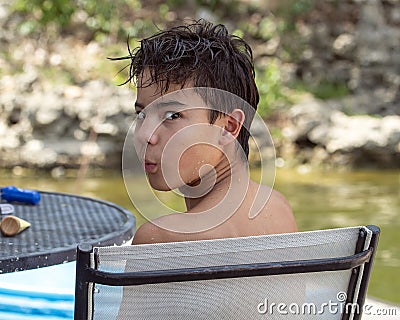 Thirteen year old Amerasian boy looking back over his left shoulder on a dock chair in Grand Lake in the State of Oklahoma Stock Photo