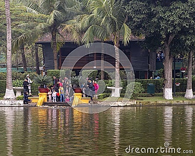Tourists feeding carp with the Stilt House of Ho Chi Minh in the background, Hanoi, Vietnam Editorial Stock Photo