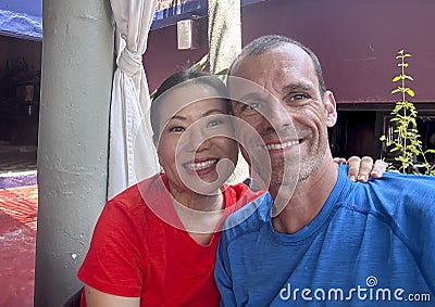 47 year-old Caucasian husband and his 57 year-old Korean wife on restaurant patio in Todos Santos, Mexico. Stock Photo