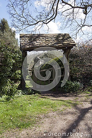 The picturesque old lychgate frames the tiny old Saxon church in spring sunshine at Duntisbourne Rouse Stock Photo