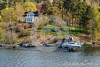 Picturesque spring coastal landscape of Stockholm archipelago with waterfront mansion and small motor boat hoisted above water on Editorial Stock Photo