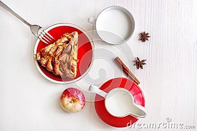 A piece of apple cake with cinnamon, fresh apple, milk cup and jug on the light wooden table. Top view Stock Photo