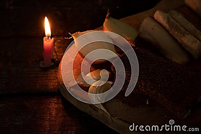 a piece of bacon, onion, garlic, black bread on a wooden table in the dark next to a burning candle, candlelight dinner Stock Photo