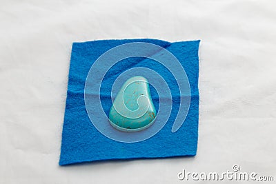 Piece of blue felt with oval turquoise bead for embroidery on white background. Handcraft, process of making of bijouterie Stock Photo