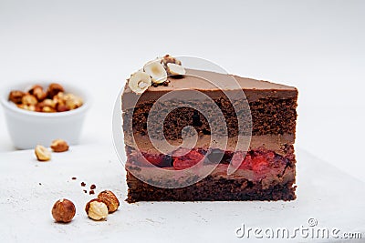 A piece of chocolate cake with cherries and hazelnut on white background. Delicious chocolate cakes on table close-up Stock Photo