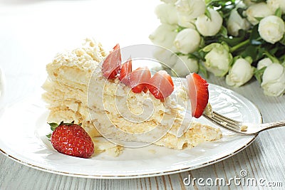 A piece of Napoleon cake on a plate adorned with a red ripe strawberry, a fork with a stuck piece of dessert Stock Photo