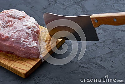 a piece of raw meat and a knife stuck on a cutting board on a dark background Stock Photo