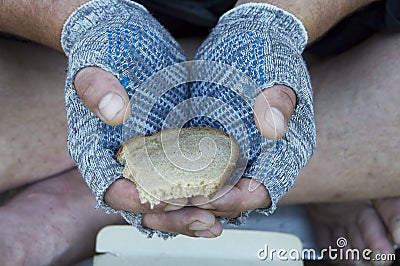 A piece of rye bread in the hands of a homeless man in gloves. Poverty, unemployment, hunger Stock Photo