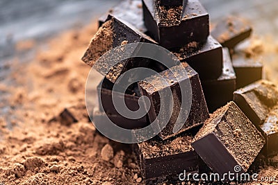 Pieces of dark bitter chocolate with cocoa powder on dark wooden background. Concept of confectionery ingredients Stock Photo