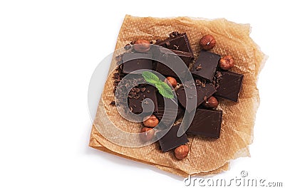 Pieces of dark chocolate, hazelnuts and mint on parchment paper, white background, isolated. View from above Stock Photo