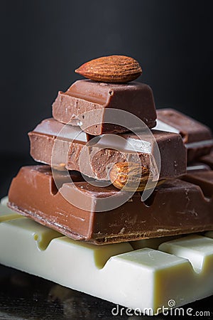 Pieces of milk chocolate with almonds and tiles of white chocolate with hazelnuts on a dark old glossy background Stock Photo