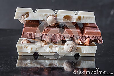 Pieces of milk chocolate with almonds and tiles of white chocolate with hazelnuts on a dark old glossy background Stock Photo