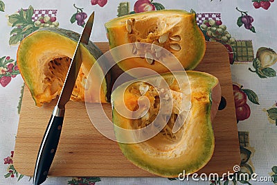 pieces of pumpkin with original yellow-green pulp on a wooden board are cut with a knife Stock Photo